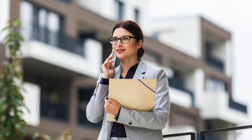 Property valuer holding a document folder, talking on the phone in front of a building