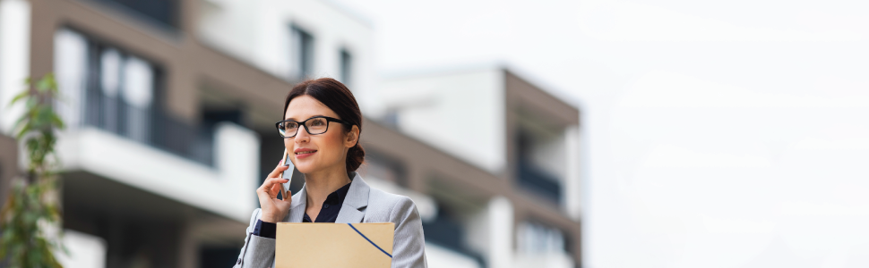 Property valuer holding a document folder, talking on the phone in front of a building