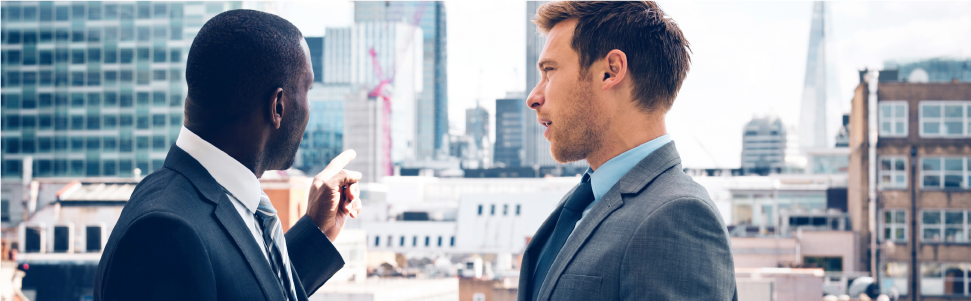 Two real estate professionals wearing suits. They are in an office, and having a discussion.
