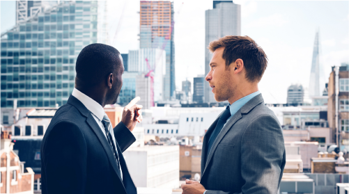 Two real estate professionals wearing suits. They are in an office, and having a discussion.